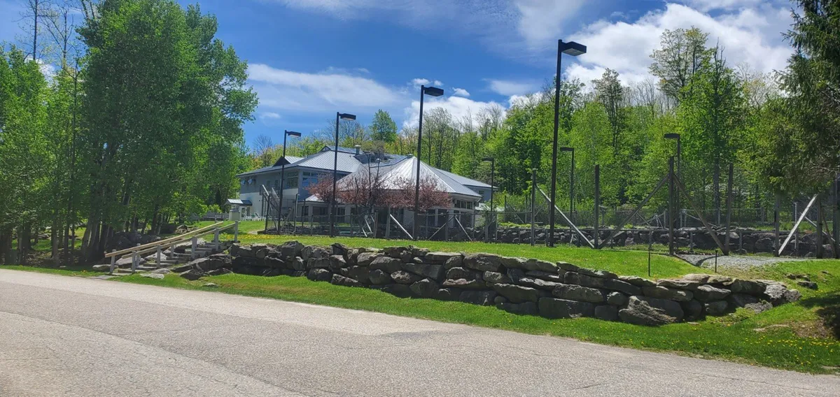 The main building is featured along a scenic pathway, bordered by rock walls and mature trees. Warmly lit, the image hints at community spaces and easy access, evoking a sense of arrival and anticipation for the relaxation awaiting inside.