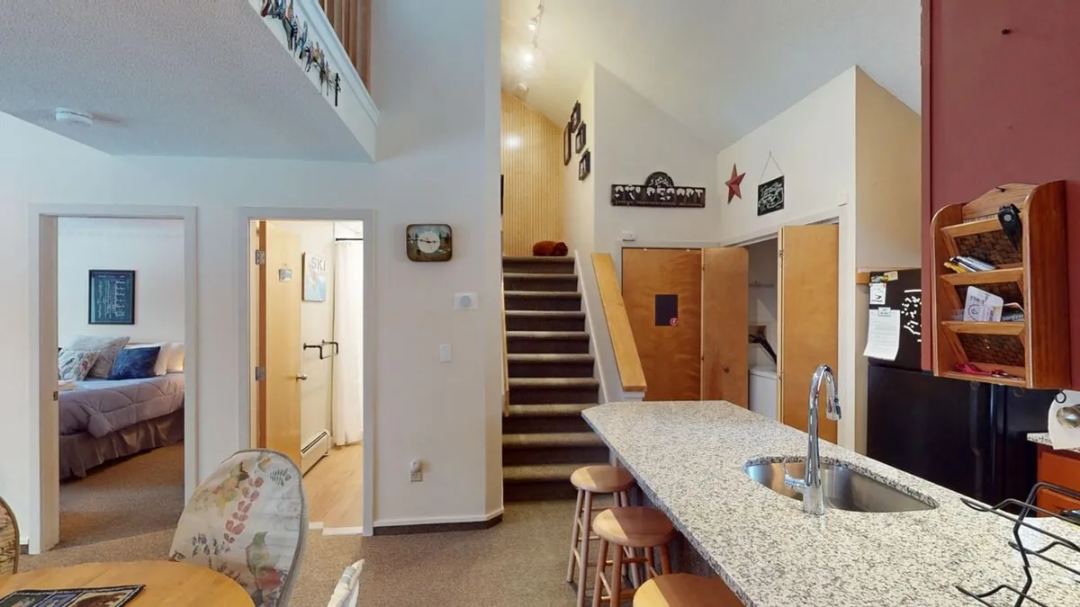A focused view of the kitchen and adjacent dining area, centered on the granite-topped kitchen island and a staircase leading upstairs. The cozy setup is ideal for cooking together and sharing stories over dinner, with the open layout encouraging family interactions.