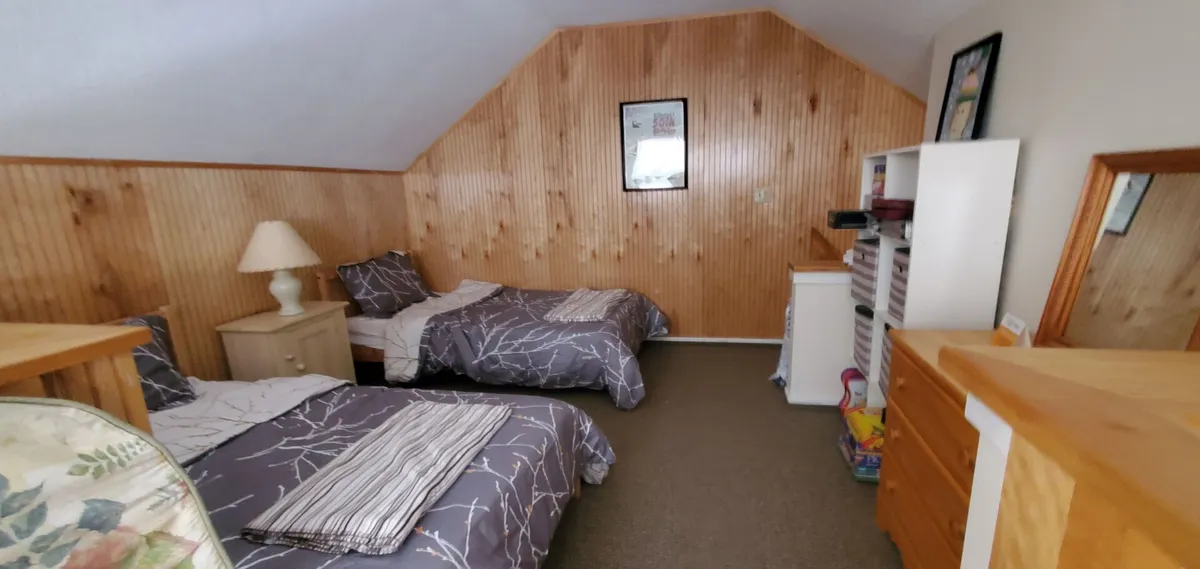 This bedroom scene showcases two twin beds with a warm wooden accent wall, soft lighting, and a dresser, offering a restful atmosphere perfect for families or groups needing flexible sleeping arrangements.