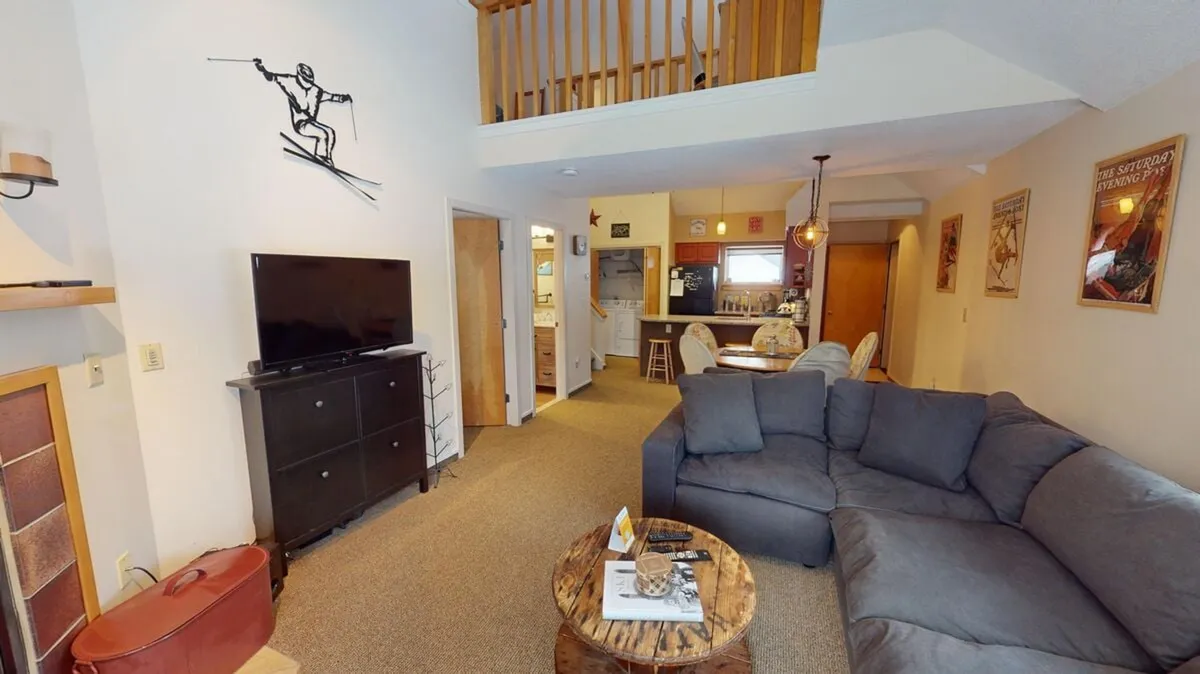 The hero image showcases a bright, open living space featuring a comfy sofa, large TV unit, inviting ski-themed artwork, and a dining area perfect for gatherings. The atmosphere feels warm and casual, ideal for relaxing after a day on the slopes or sharing meals with loved ones.