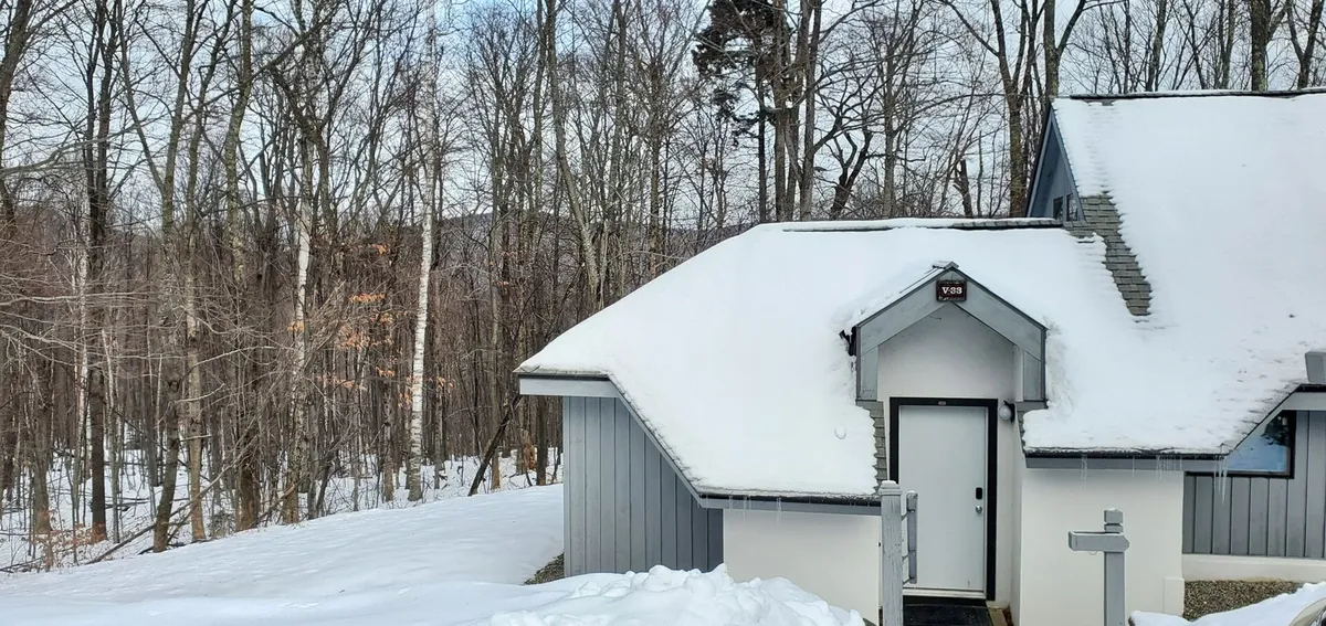 A serene winter exterior of the property, featuring a snow-covered roof and a wooded backdrop. The inviting front door hints at warmth inside, while the setting places the home squarely within Killington’s scenic, activity-rich landscape.