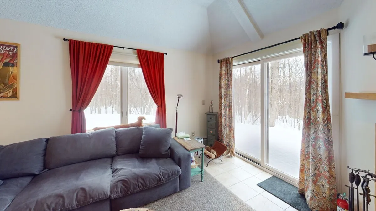 A cozy living area with a sofa facing large windows, offering a wooded view. The ambiance is warm and welcoming, perfect for relaxing with morning coffee or enjoying evening chats by the fireplace. The setup encourages both relaxation and social moments.