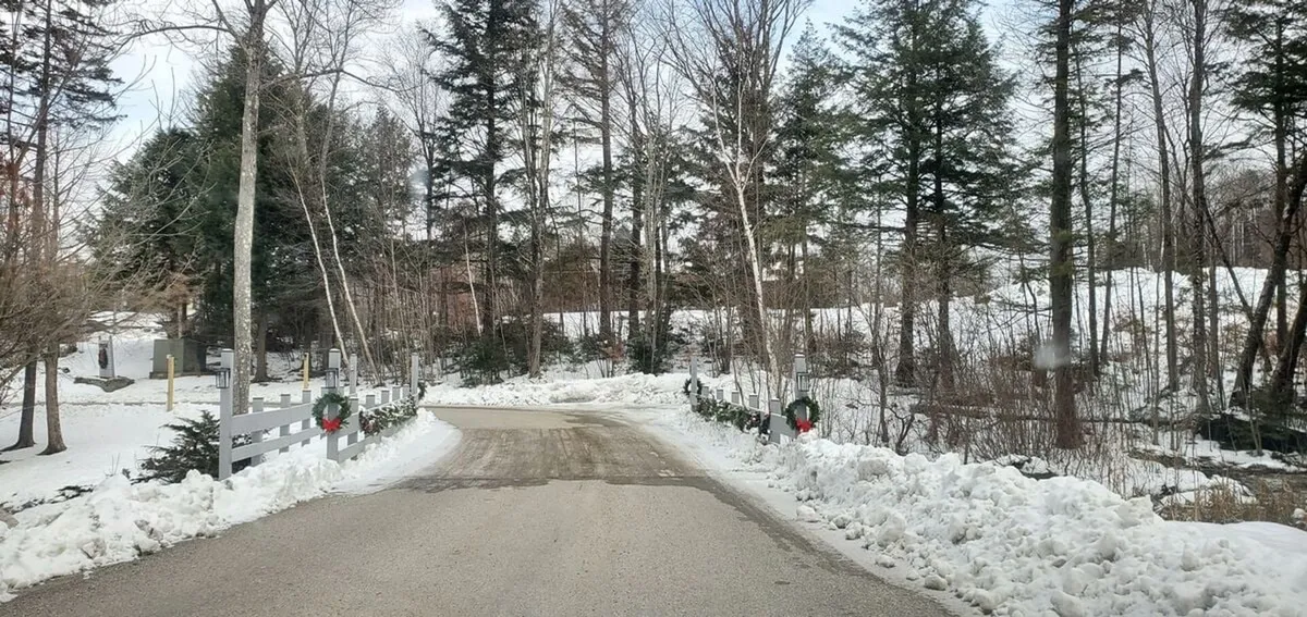 A peaceful snow-lined road bordered by trees and festive wreaths on the fence. The image evokes a sense of community and seasonal celebration, reinforcing the area’s welcoming atmosphere and easy access to local experiences.