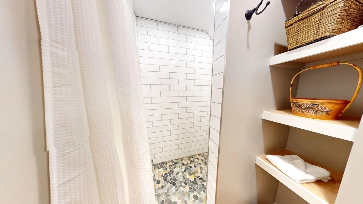 A beautifully renovated bathroom space featuring a modern shower area with a textured stone floor, thoughtful baskets on shelves for storage, and a spa-like, calming aesthetic. The room feels like a soothing retreat for self-care routines.