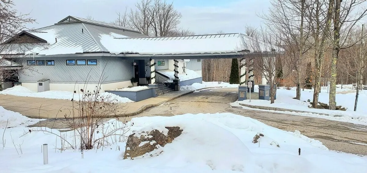 A wide exterior shot highlighting the modern architectural design of the building set against a snow-covered landscape, with the carport area visible. The serene winter scene emphasizes easy access and arrival, conveying the tranquility and excitement of staying so close to the winter action.