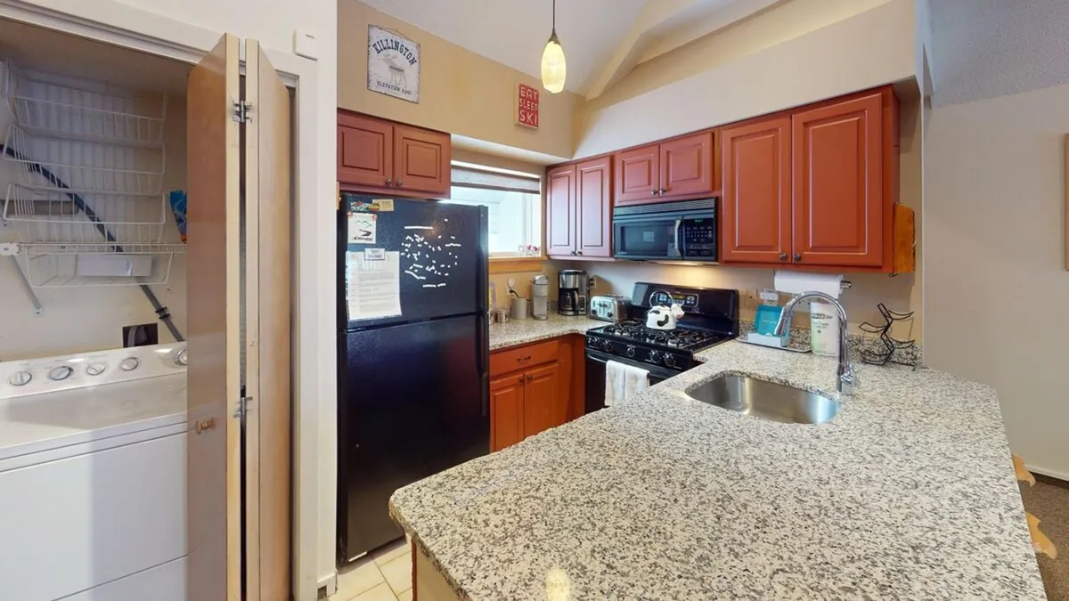 This image features a spacious kitchen with granite countertops, bold red cabinetry, and sleek stainless steel appliances. The setup invites guests to cook, socialize, and gather for shared meals, reflecting a heart-of-the-home vibe.